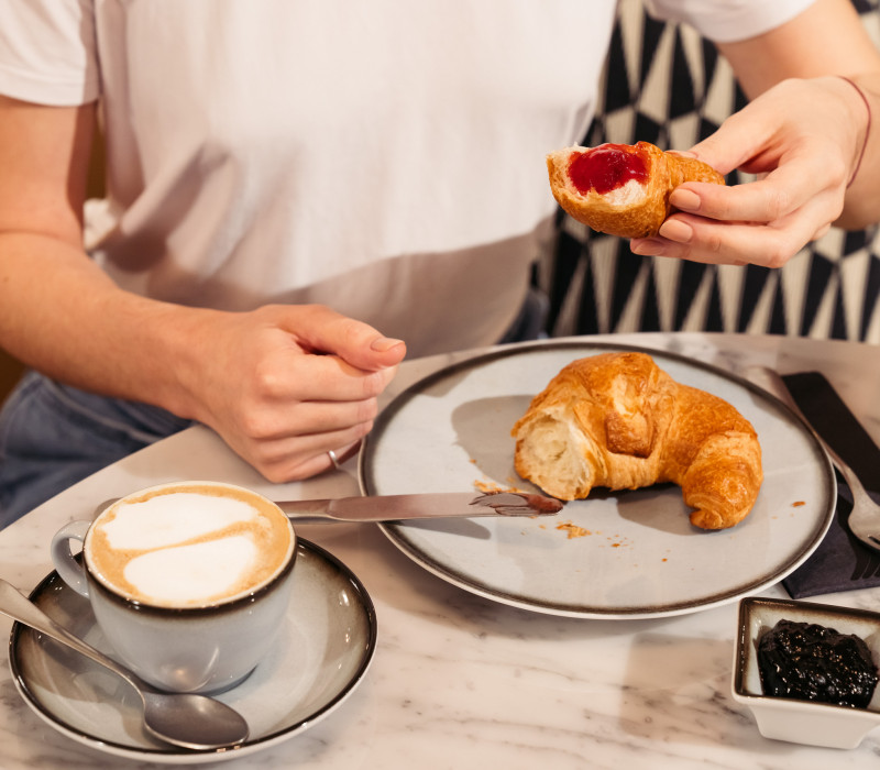 Frau hält beim Frühstück im Hotel im Wiener Zentrum ein Croissant mit Marmelade in der Hand